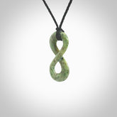 This piece is a fine, delicate eternity shaped pendant. It was carved from a lovely green piece of nephrite jade. It is suspended on an black braided cord that is length adjustable.